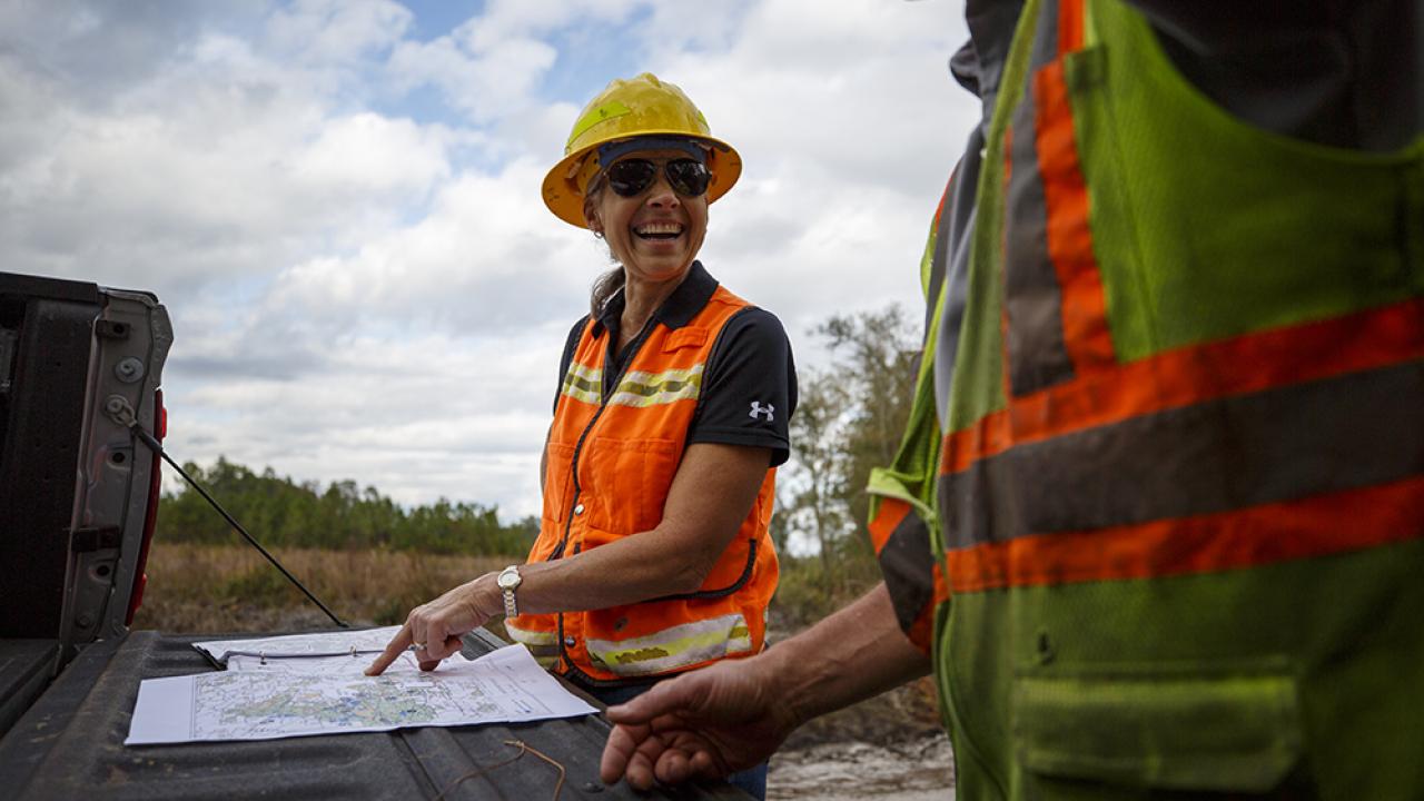 Terri Hall points to a map laid on the tailgate of a truck, smiling at another crew member