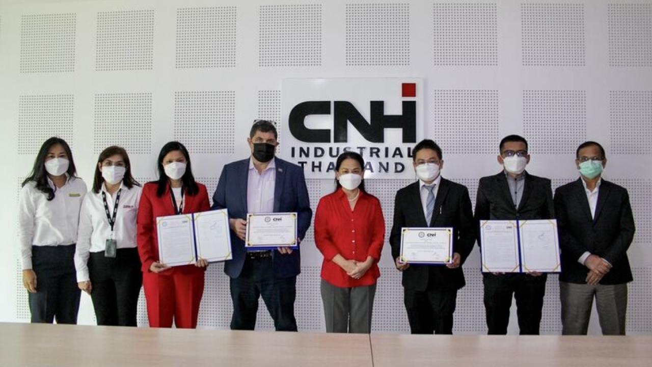 Group of people, all wearing protective masks, stand in front of CNHI sign in a conference room. Some hold documents