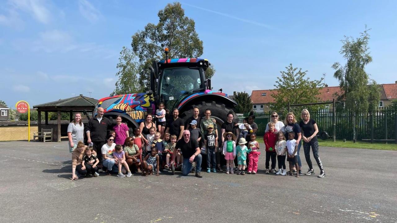 A large group of children and adults stood together in front of a colourful tractor