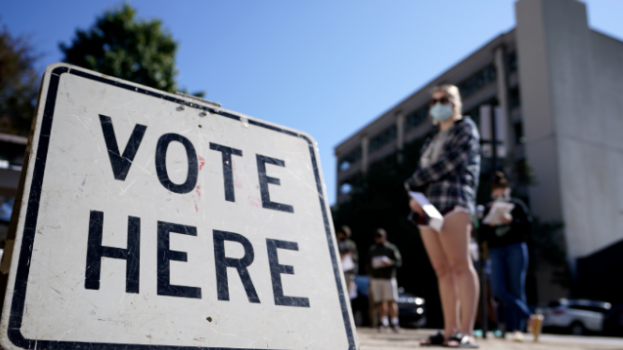Woman stands if front of a Vote Here sign.