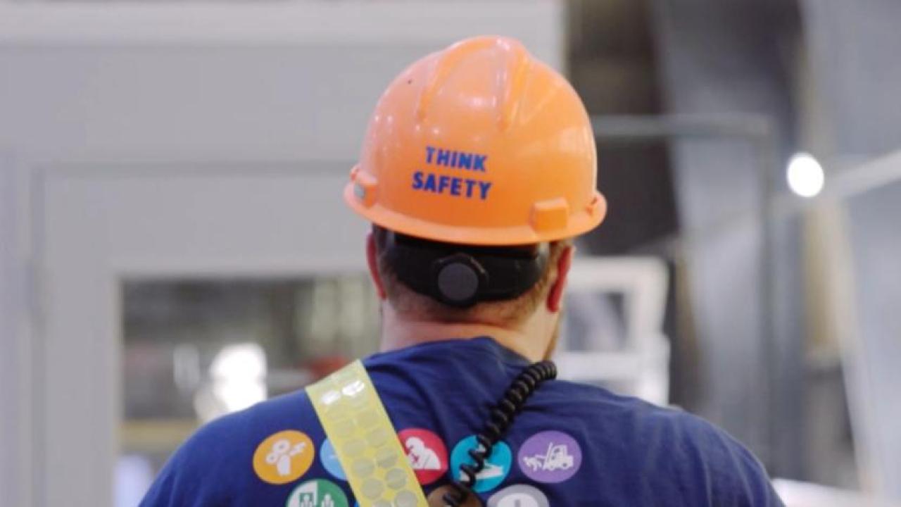 A person walking away, "Think Safety" on the back of their hard hat.