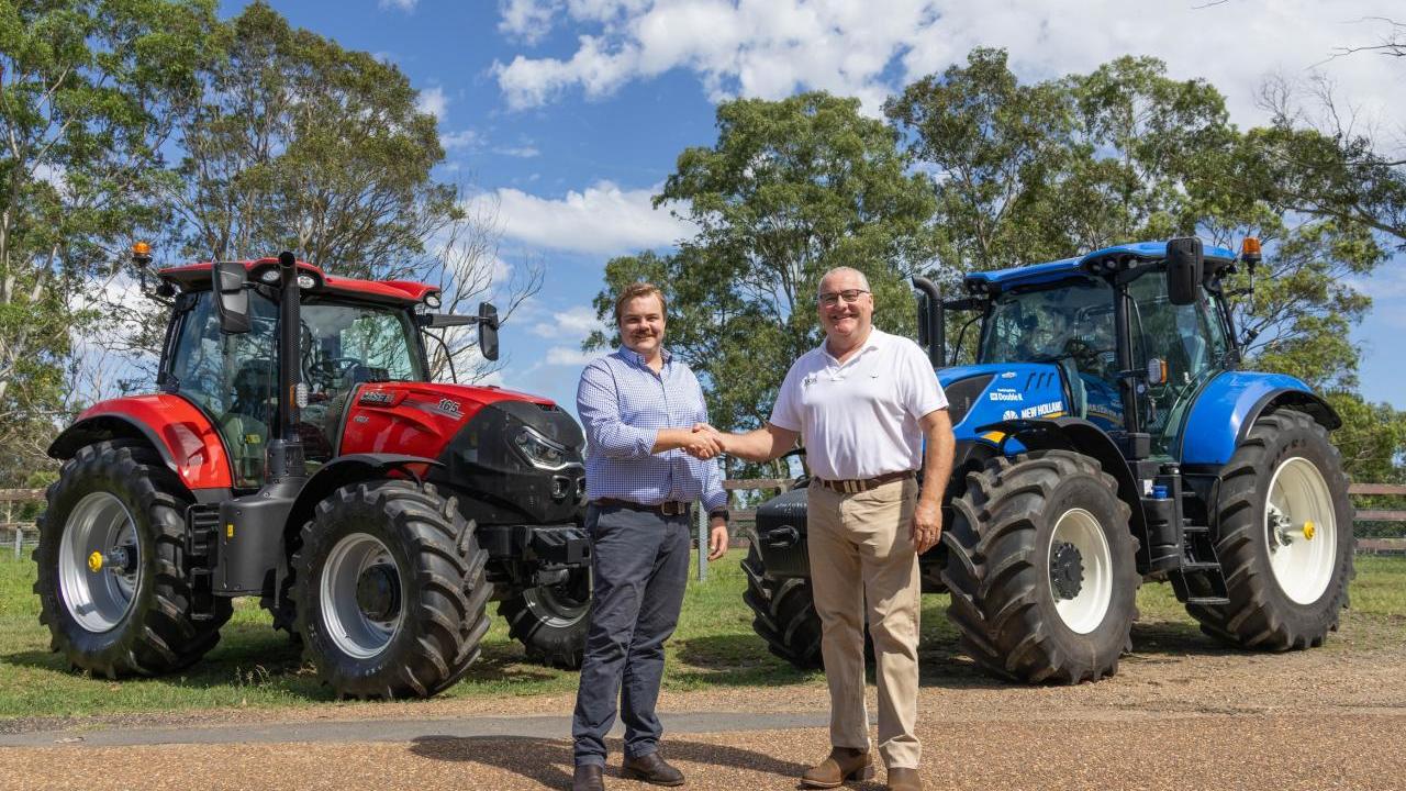 Two people shaking hands in front of two farming tractors outside.