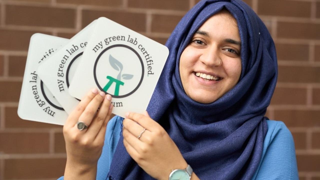Woman holding stickers that say, "My Green Lab Certified"