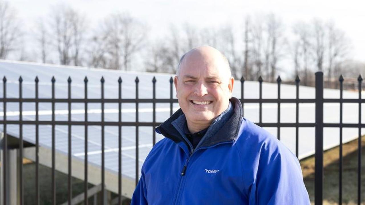A person standing in front of a fenced-off solar panel field