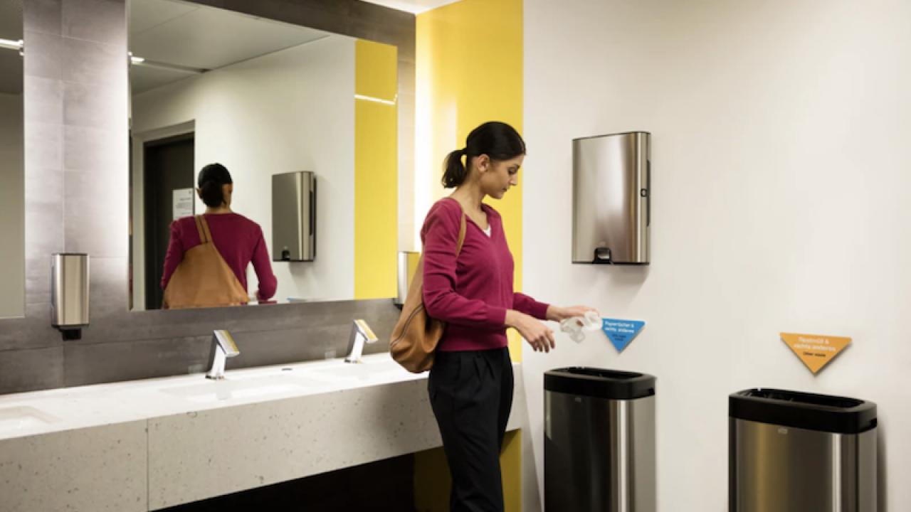 A woman standing in a bathroom using a paper towel.