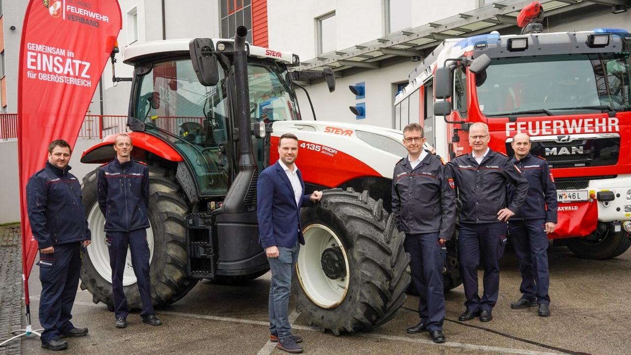 Six people stand arounf a large tractor and fire truck outside.