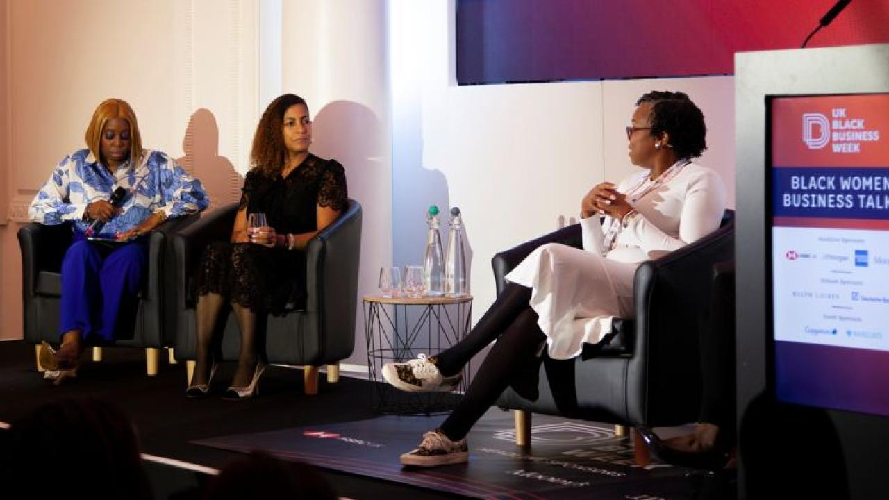 Three people seated on a stage, talking