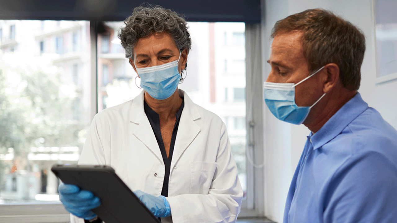 Healthcare professional and another person wearing face masks while looking at a tablet pc