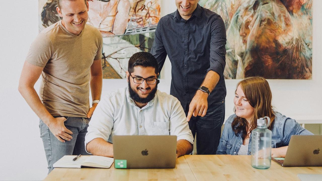 Four coworkers at a table working with laptops.