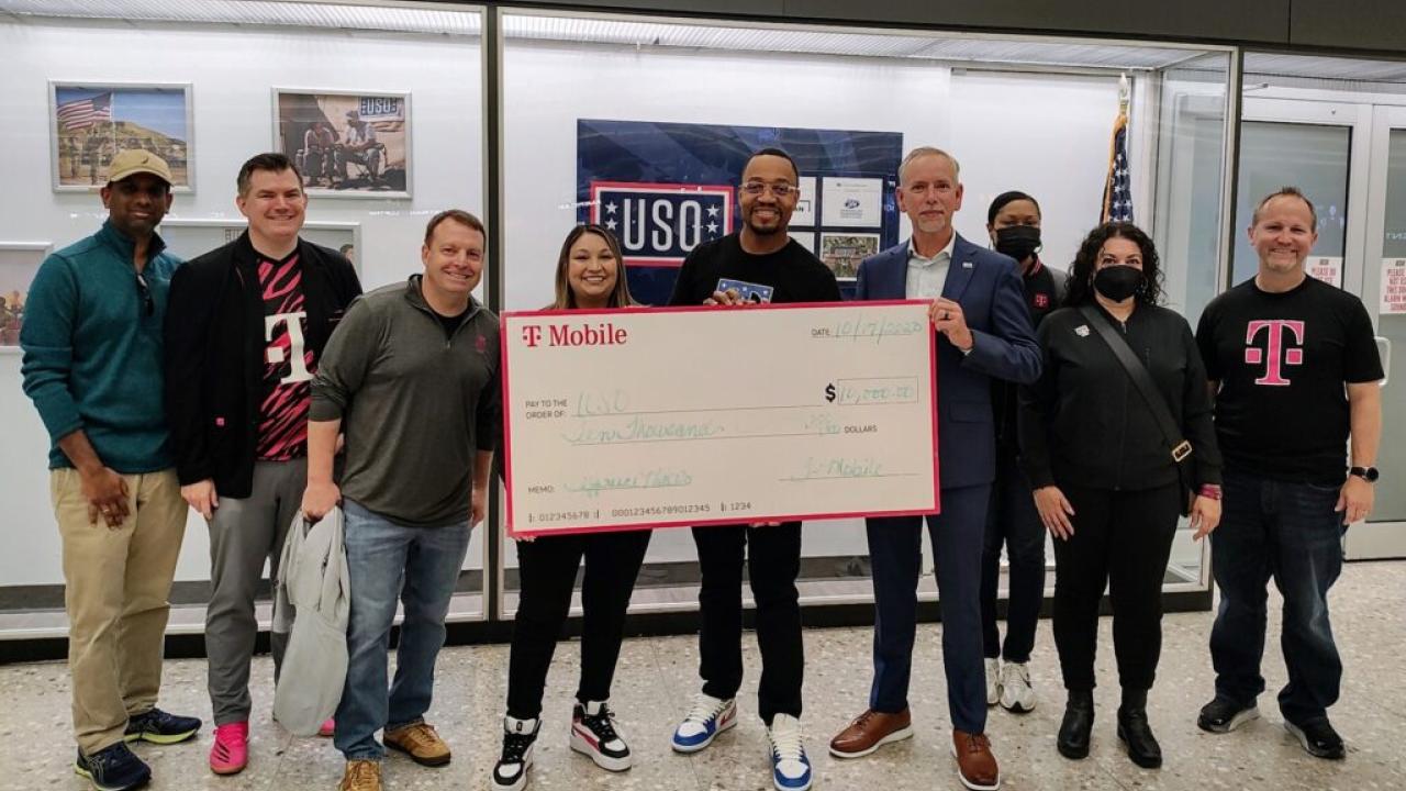 A group of people posed with a large check. USO sign behind them.