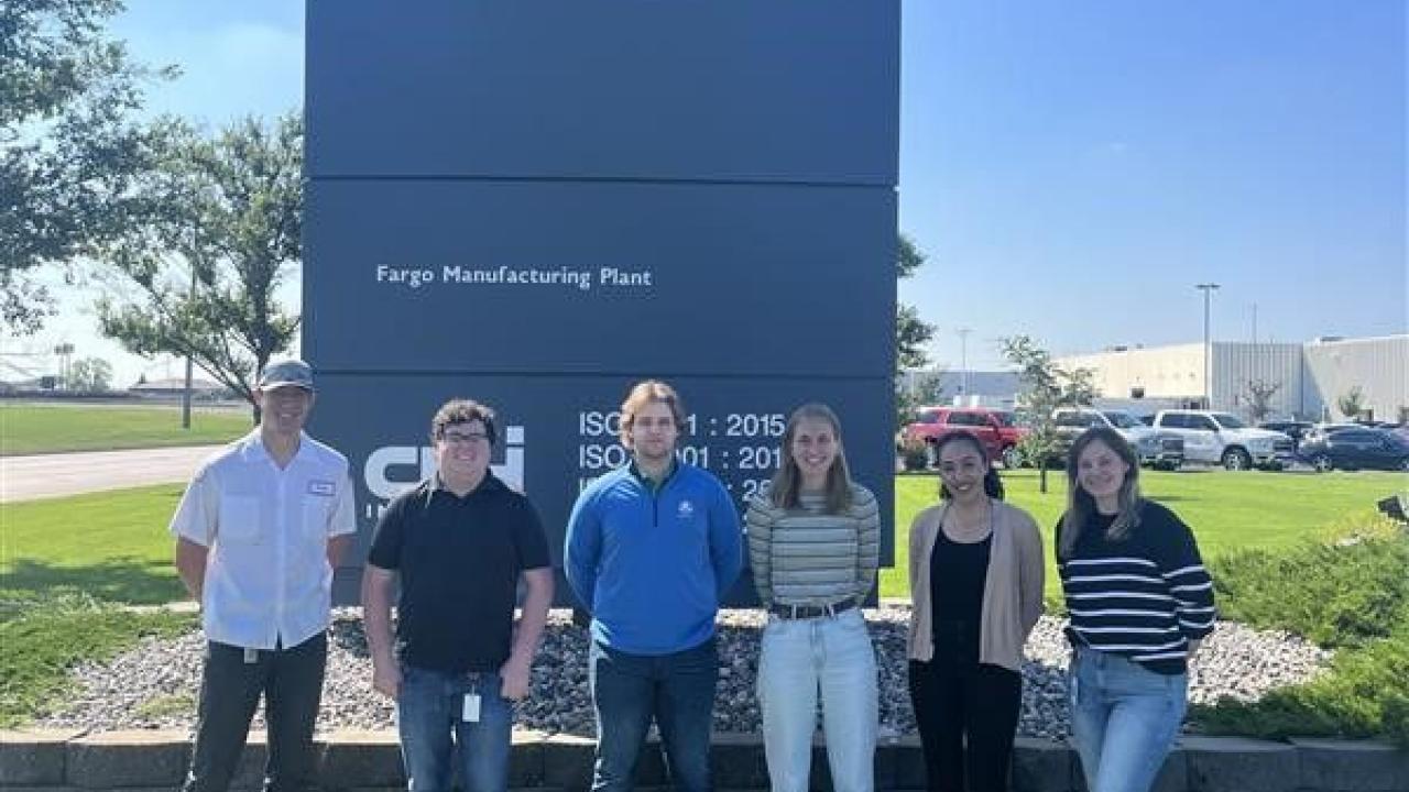 Six people posed outside in front of a tall sign for Case.
