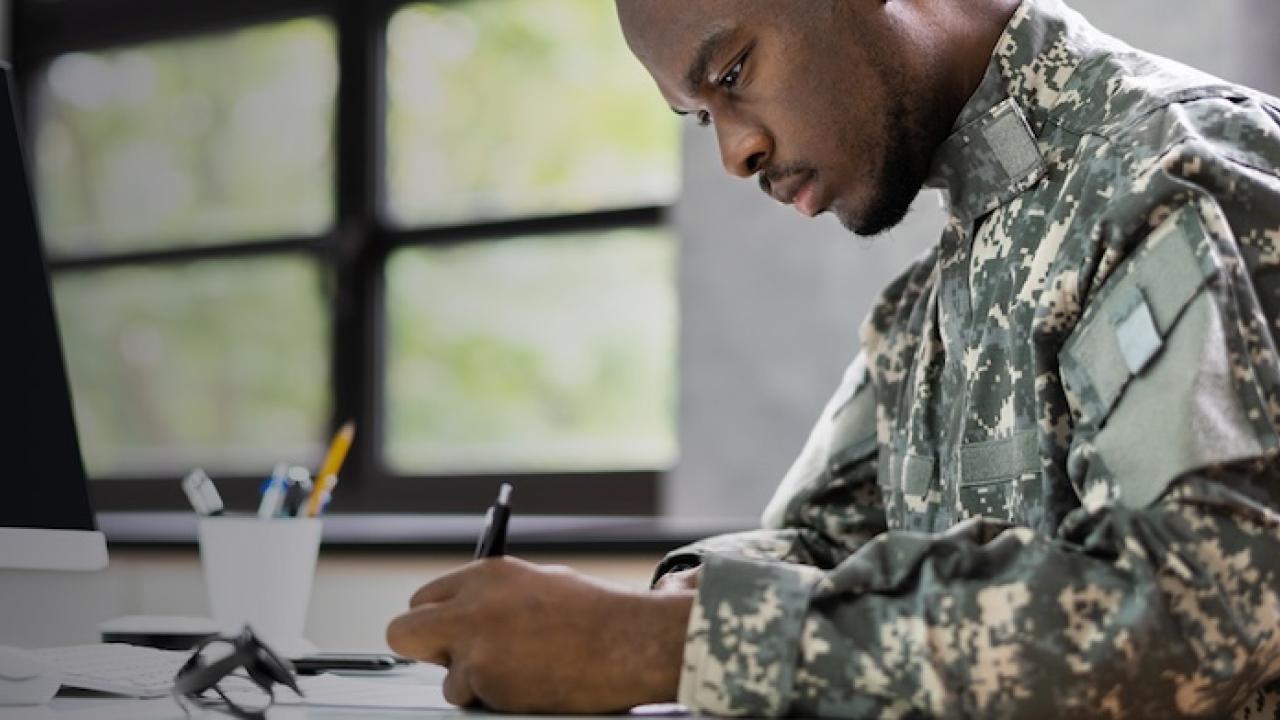 Male military individual seated at a desk wearing fatigues.
