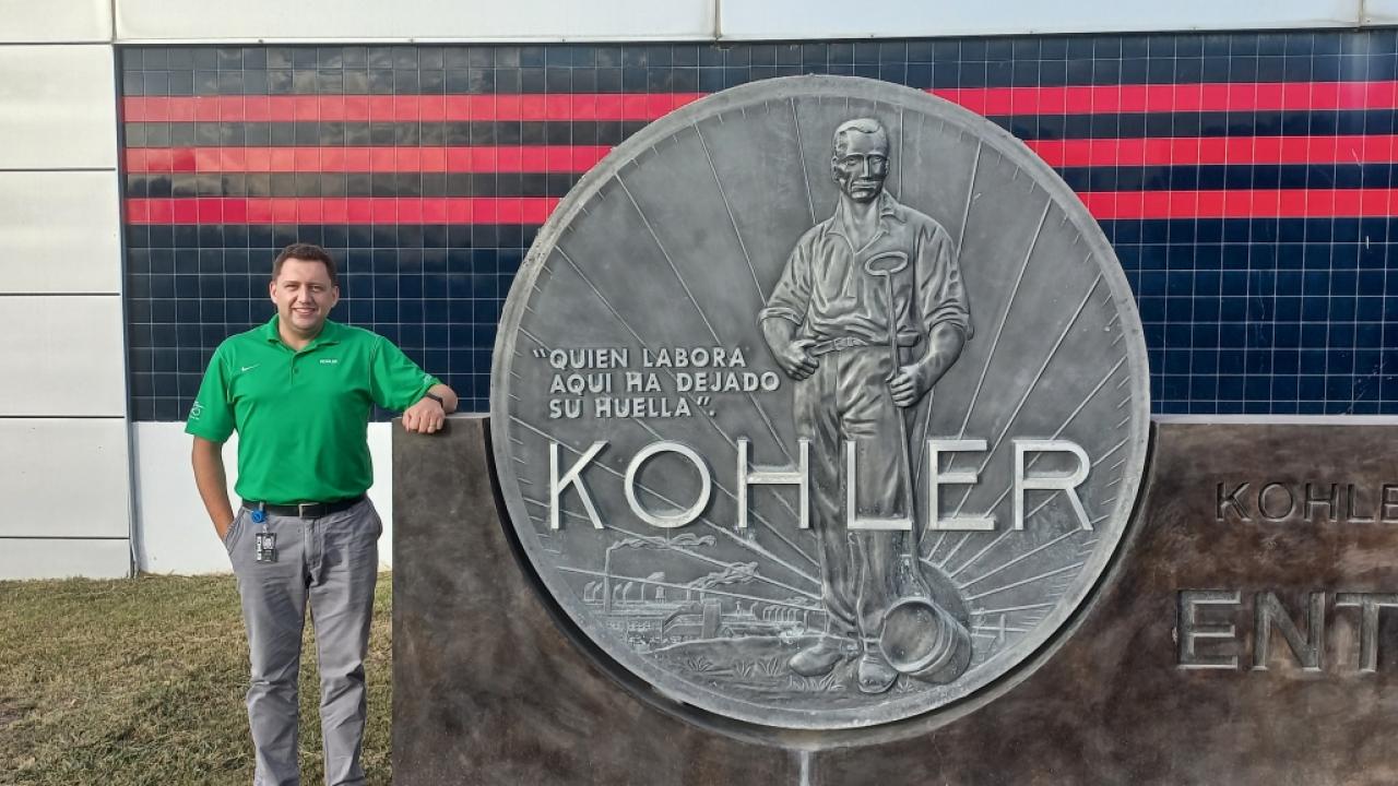 Vitor Wojastyk standing next to a large sign at the entrance of the Kohler plant