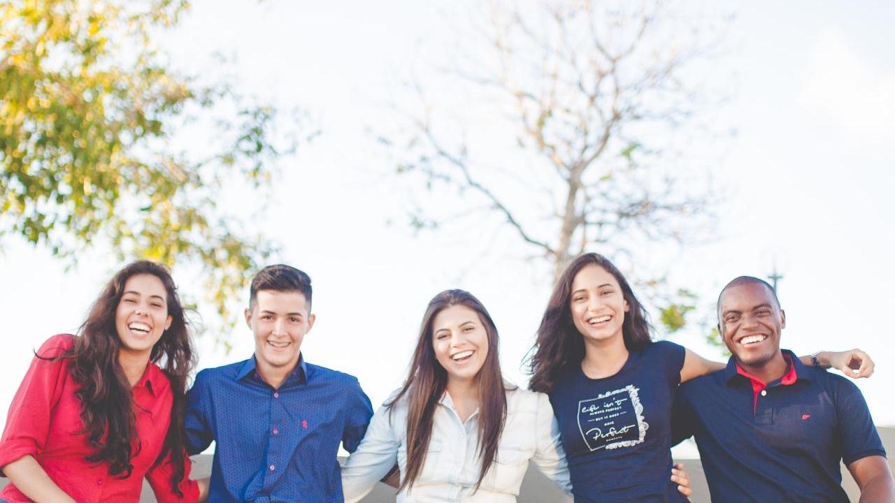 A group of five people sitting on a bench with arms around each other.