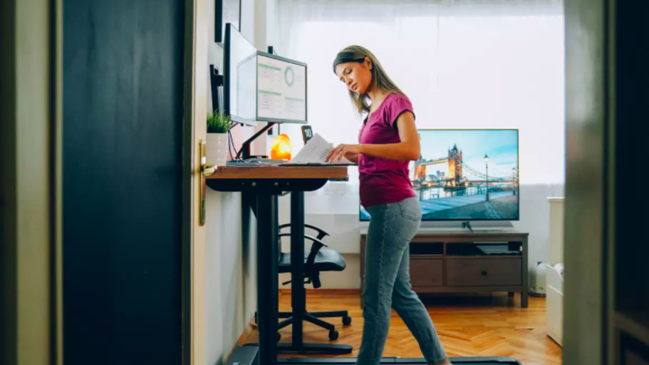 Woman at standing desk with walking treadmill underneath 