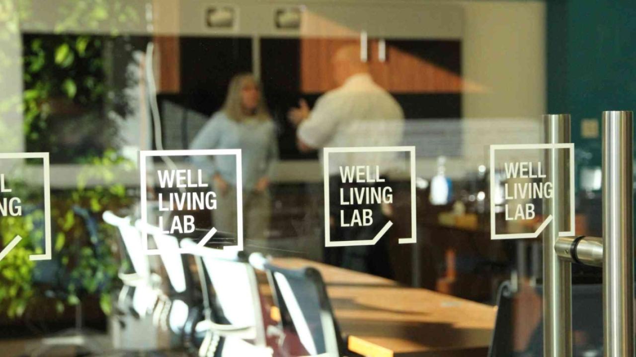 looking into the Well Living Lab from outside glass walls, two people talking inside
