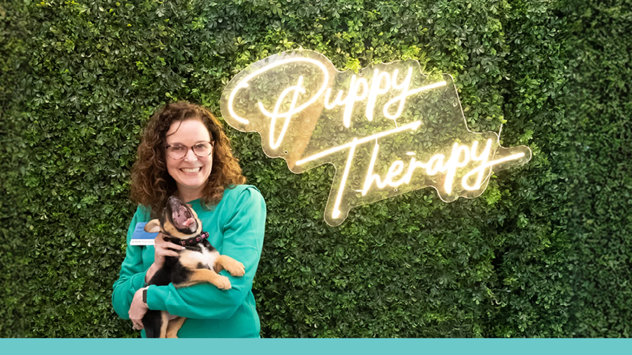 Woman holding dog with the words, "Puppy Therapy" behind them