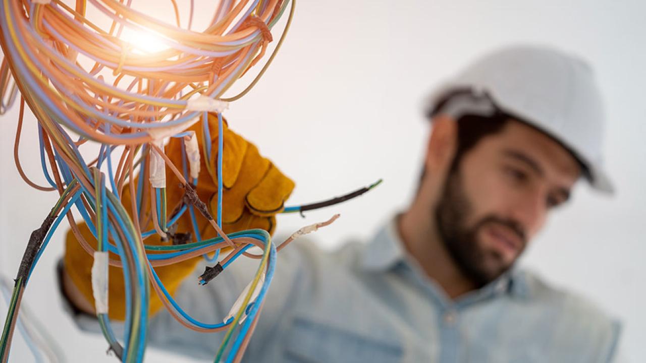 Electrical worker shown wearing a helmet and working on wiring.
