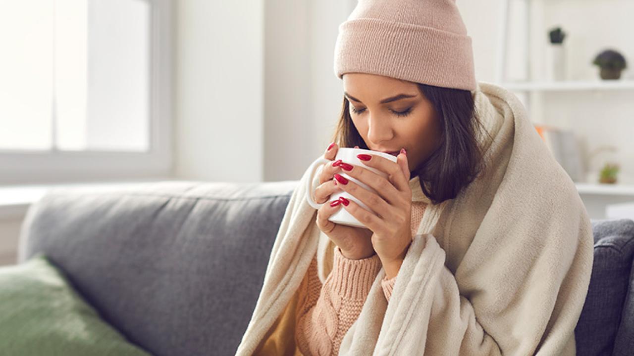 women drinking from a mug wrapped in a hat and blanket