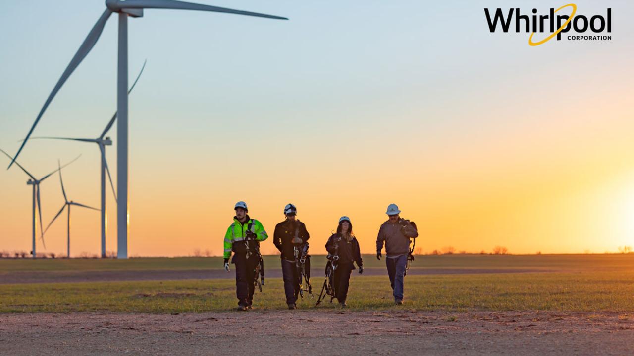 four workers in safety gear walking in front of wind turbines at dawn