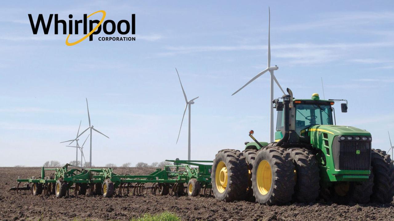 A large green tractor tills a field, wind turbines behind it in a row. Whirlpool logo in the upper left.
