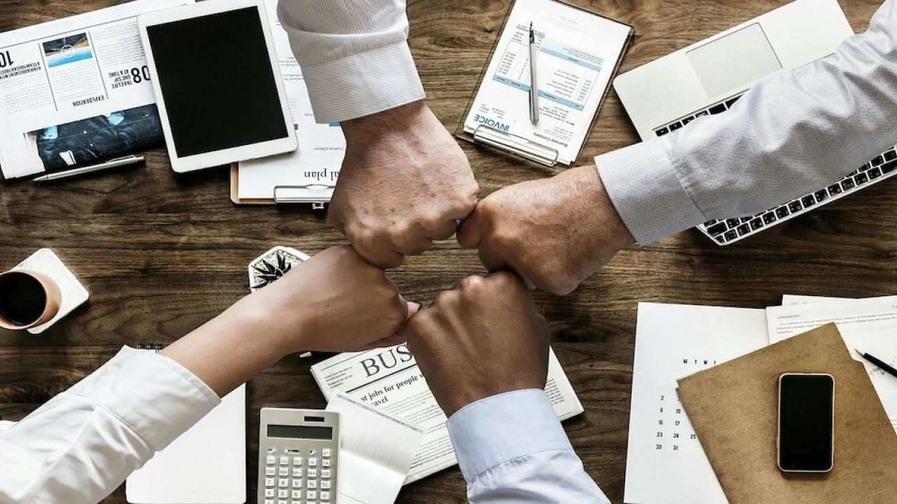 Four people fist bumping over a table at work.