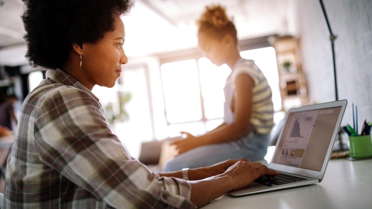 woman working on a laptop with a child in the background