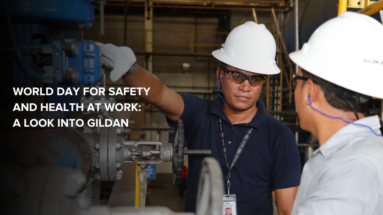 Two Gildan employees wearing safety equipment, interacting on the factory floor