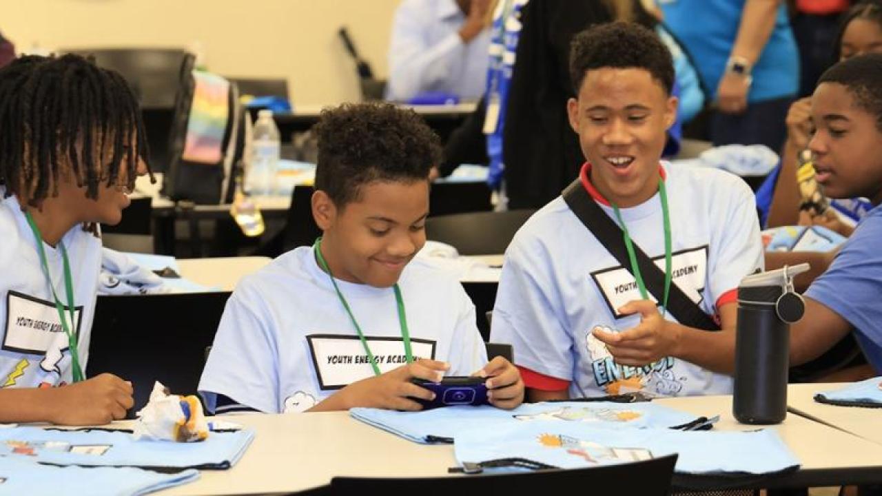A group of kids in matching shirts talking and smiling, seated at a long table.