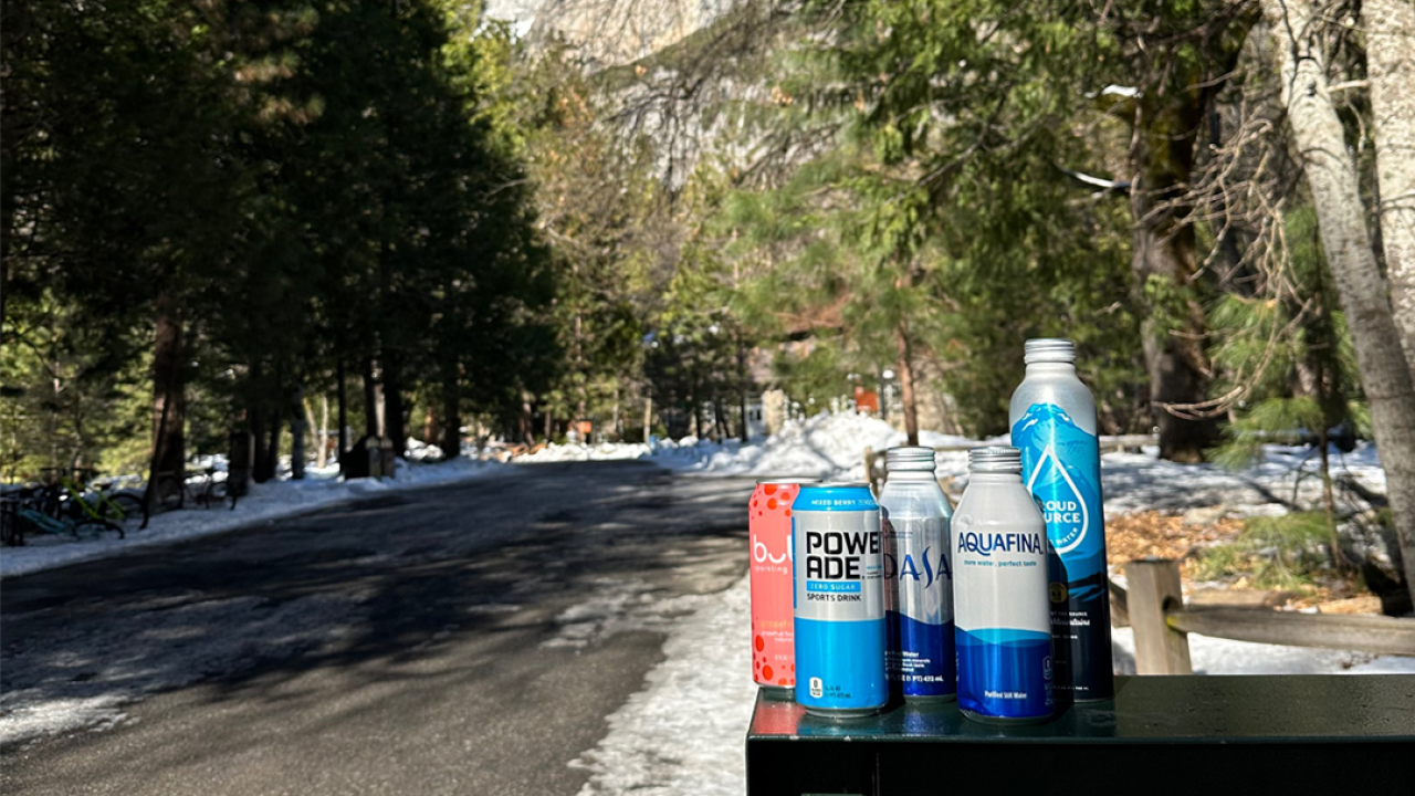 Recyclable bottoms on top of a mixed recycling bin. In the background are mountains and trees. 