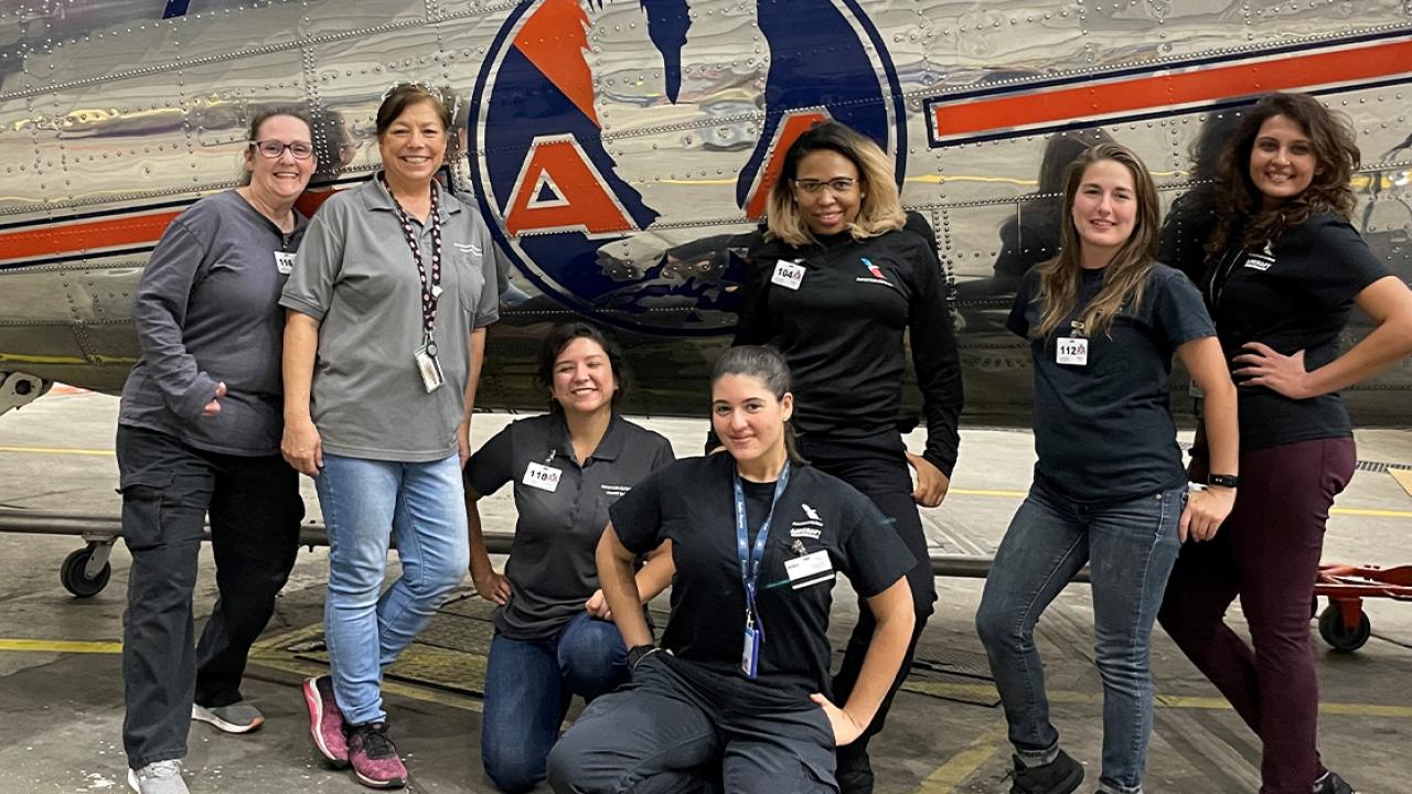7 women standing with a plane