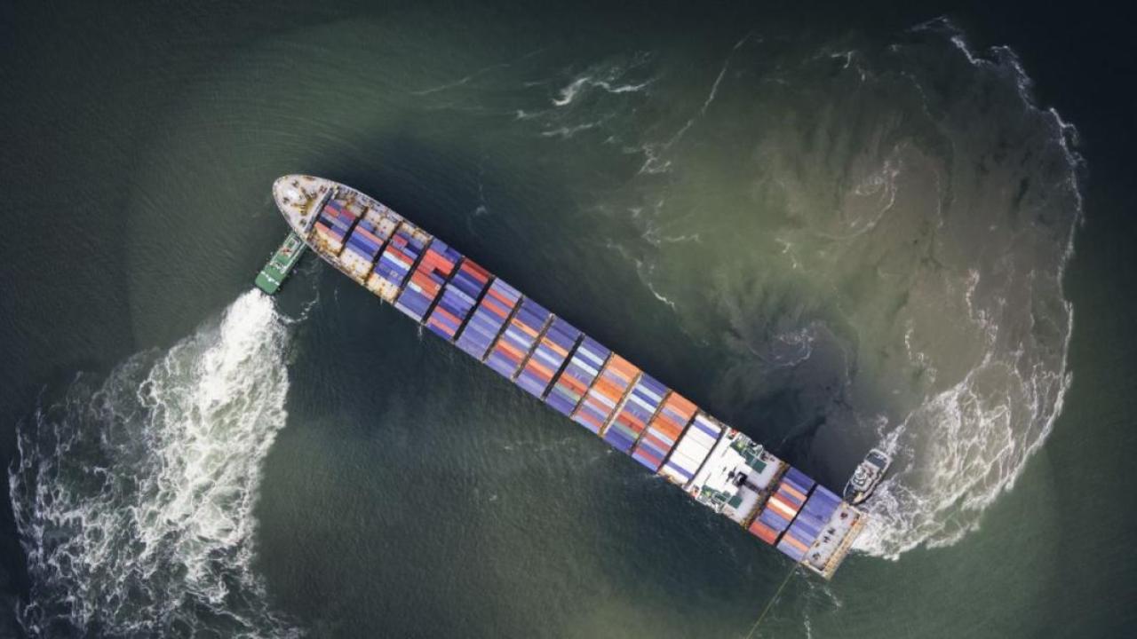 Two small boats moving a container vessel.