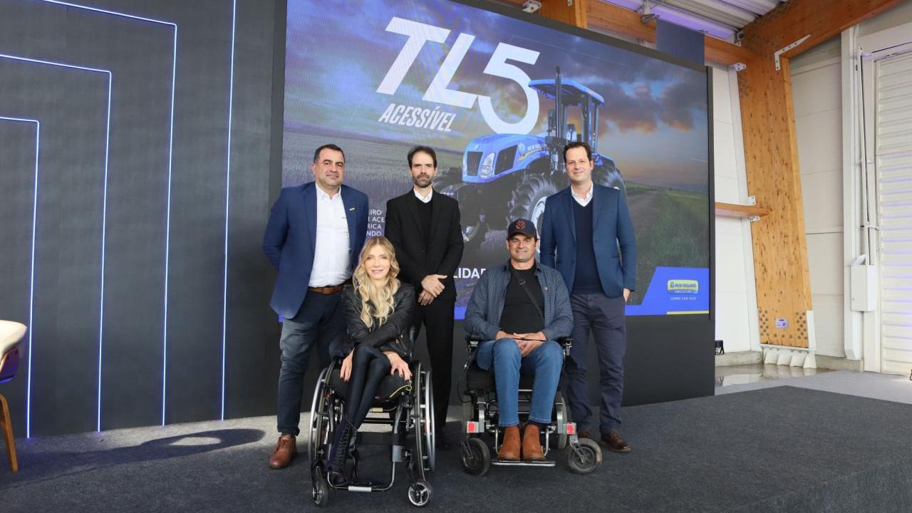 Three people standing behind two people in wheelchairs with a picture of the the Accessible New Holland TL5 tractor on the wall behind them