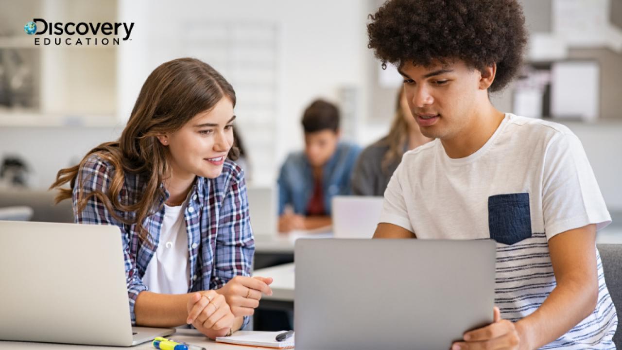Two students looking at a laptop screen in a classroom