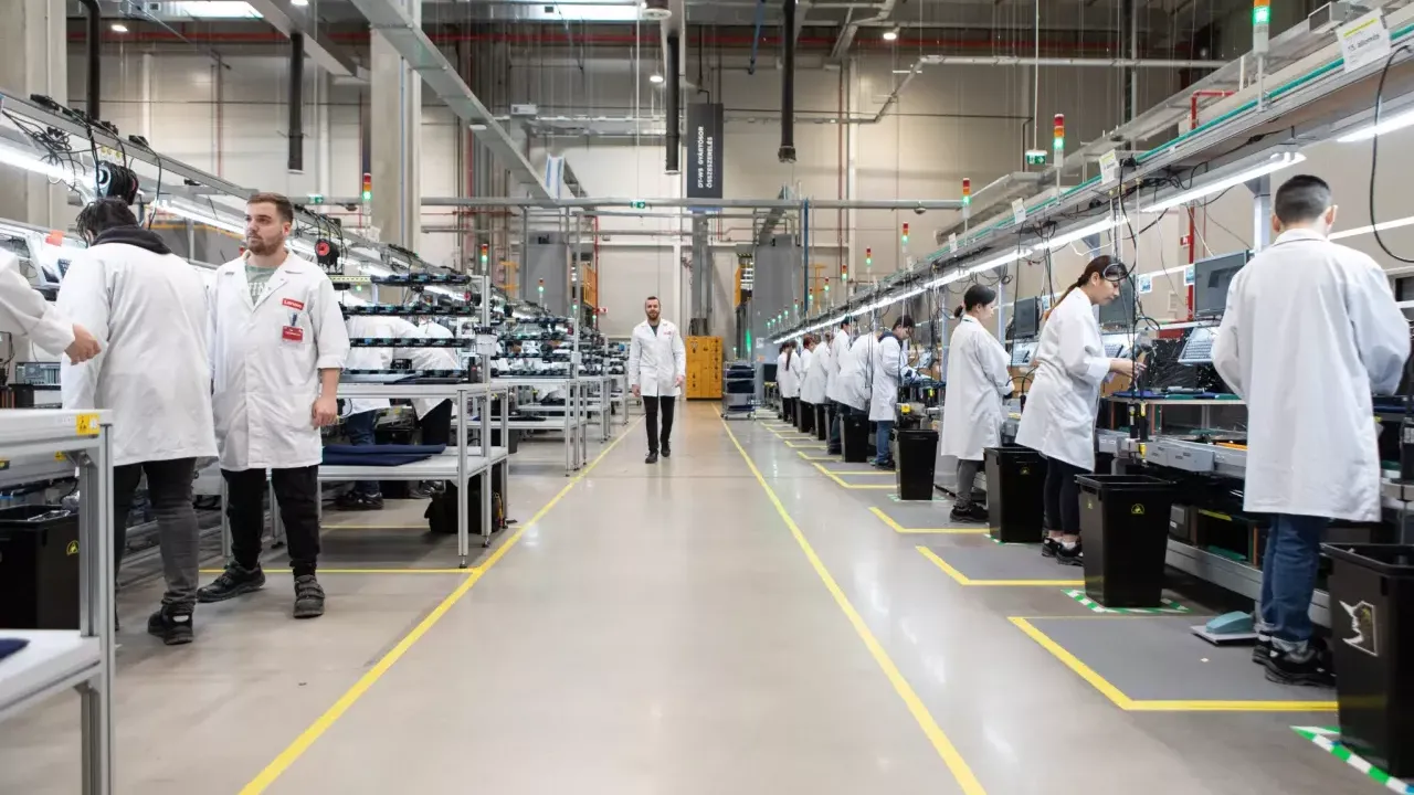 Long view at a manufacturing plant. People working on both sides of an aisle.