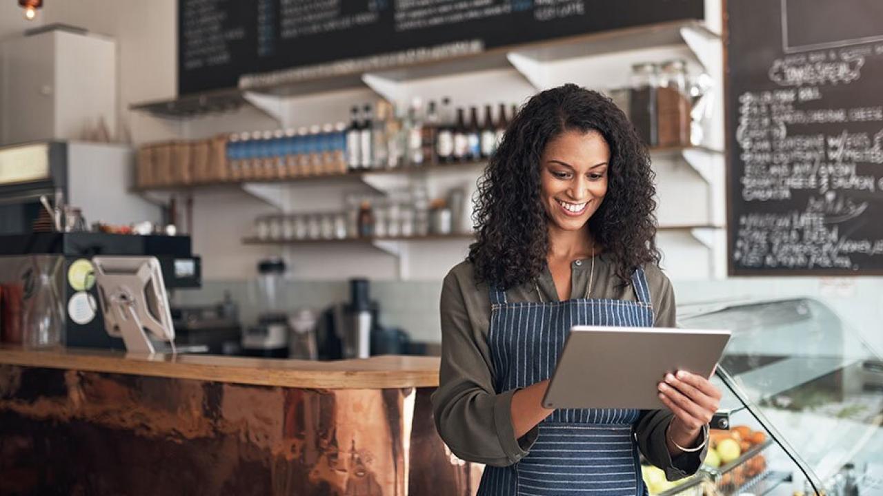 A smiling person works on a tablet device in a cafe setting.