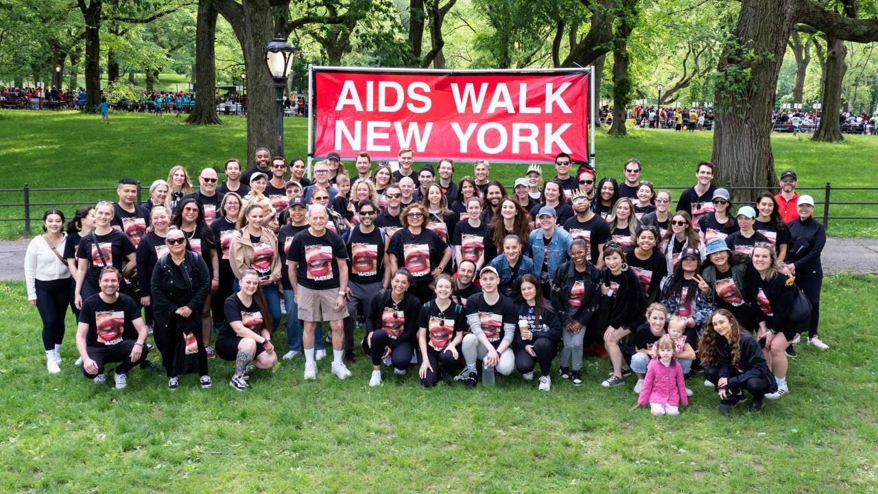 The MAC team of walkers in a park in front of "aids walk new york" sign.