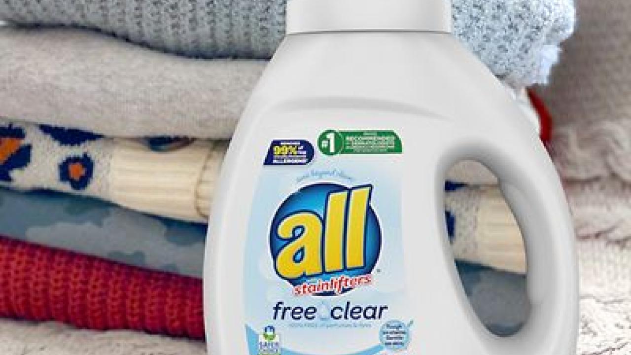 A bottle of All detergent and a stack of folded laundry behind it.