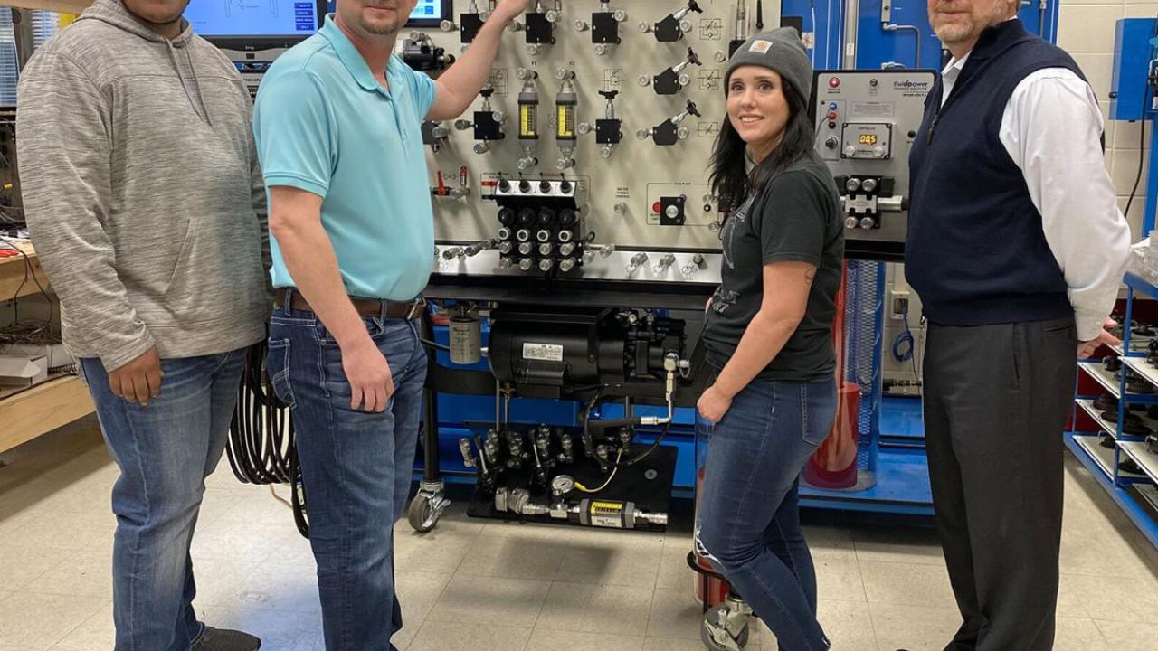 Four people in front of manufacturing equipment