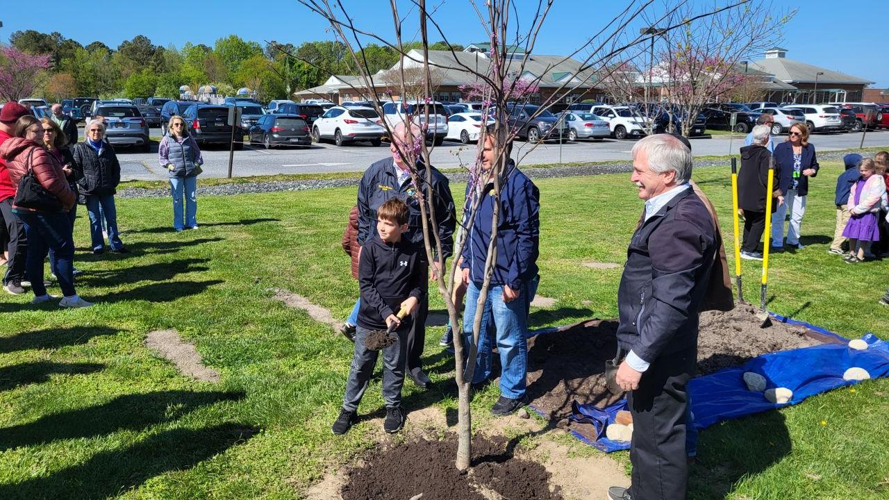 A child putting dirt on a planted tree as adults look on.