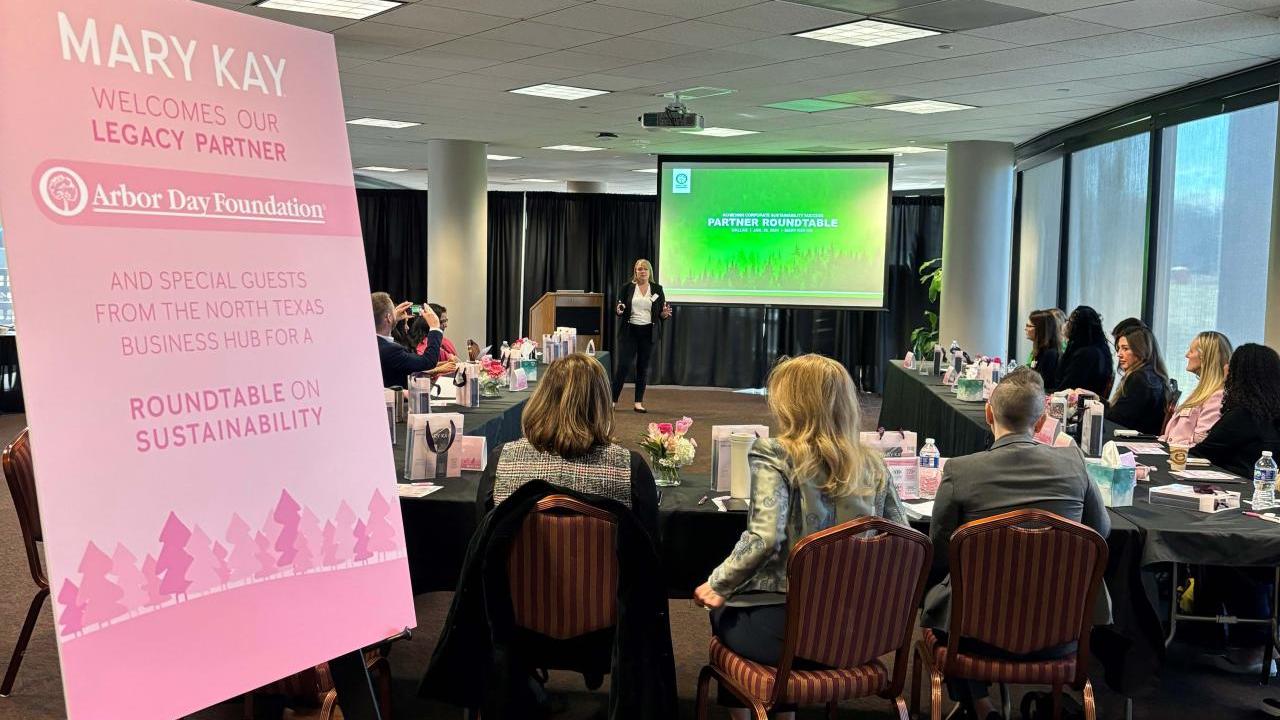 People seated in a conference room a sign "Mary Kay welcomes our legacy partner Arbor Day Foundation."