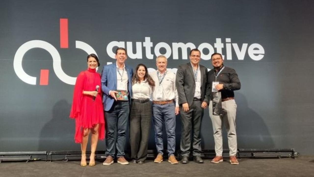 A row of people posed on a stage in front of a sign "Automotive". One holds an award.
