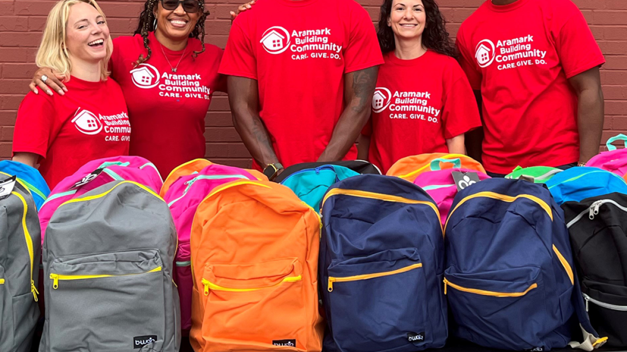 Volunteers stand behind a table of backpacks