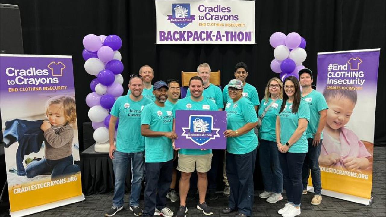 A group of volunteers posed together, some holding a sign "Cradles to Crayons" signs to the sides and behind them for Cradles to Crayons and Backpack-a-thon.
