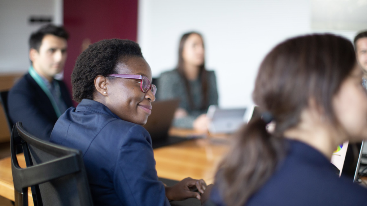 People in business attire gathered around a conference table and smiling