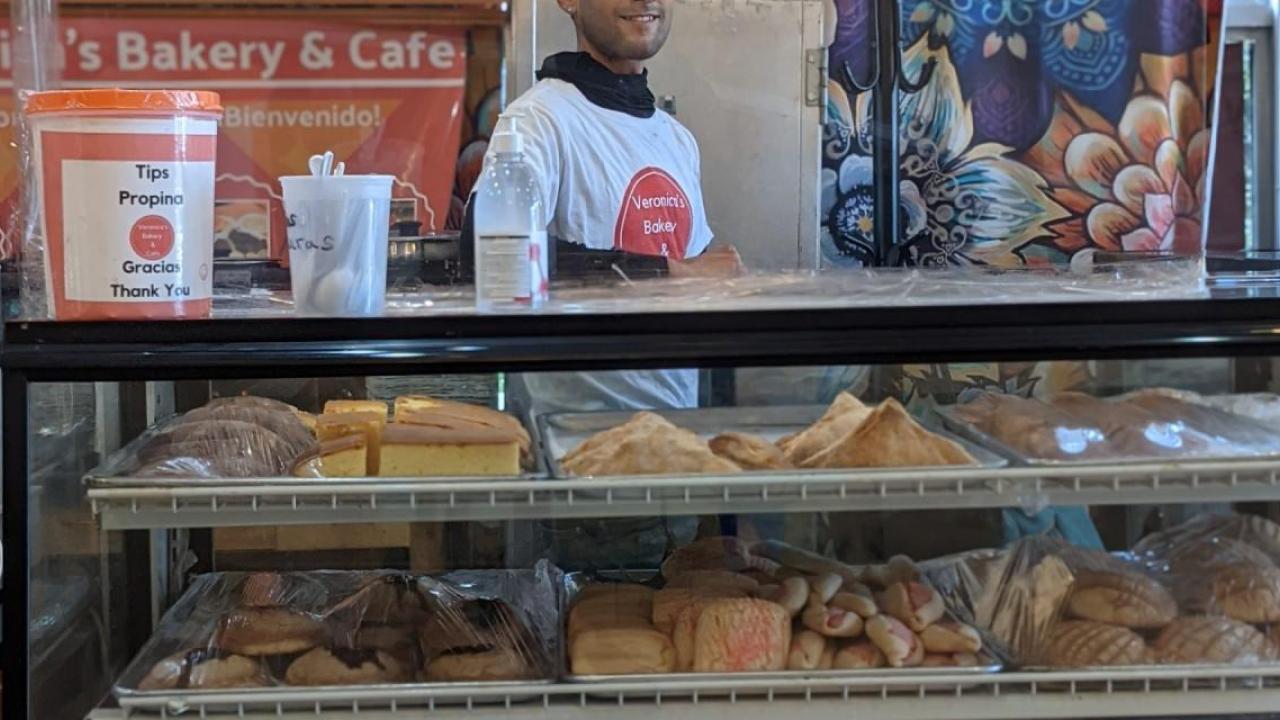 An employee behind a display case filled with bakery items.
