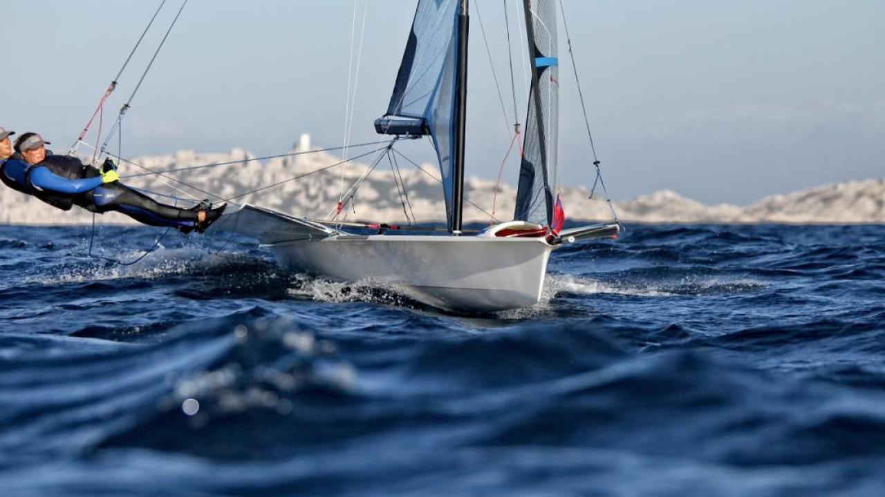 Two people leaning far out of a sailboat on open water.