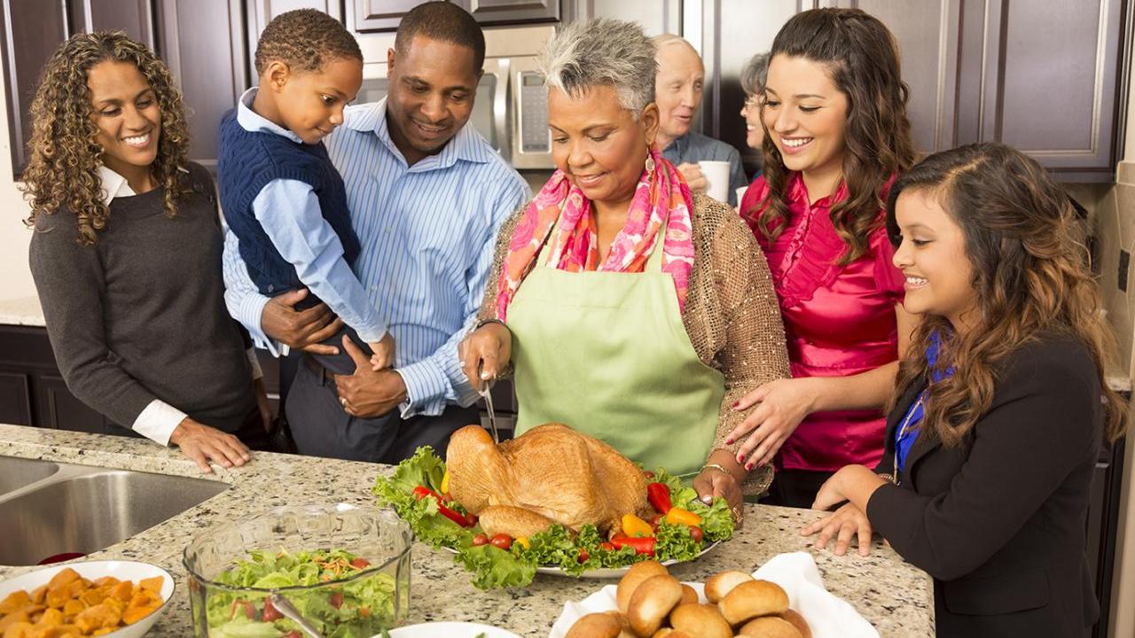 A smiling family collected around a Thanksgiving turkey being carved