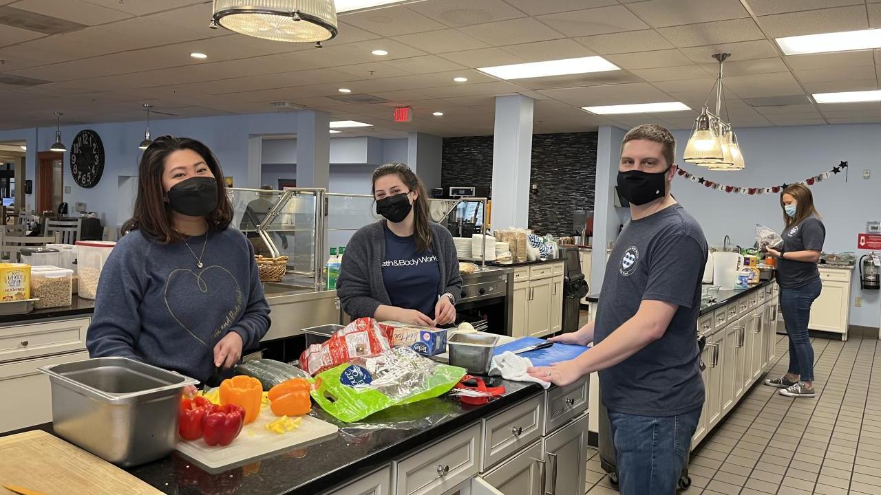 Four Bath & Body associates stand at long counter in the Ronald McDonald House preparing fresh vegetables.