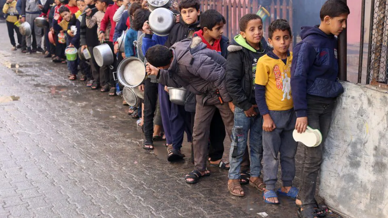Palestinian children carry pots as they queue to receive food cooked by a charity kitchen, amid shortages in food supplies, as the conflict between Israel and Hamas continues, in Rafah in the southern Gaza Strip December 14, 2023./ Photo by Saleh Salem for Reuters. 
